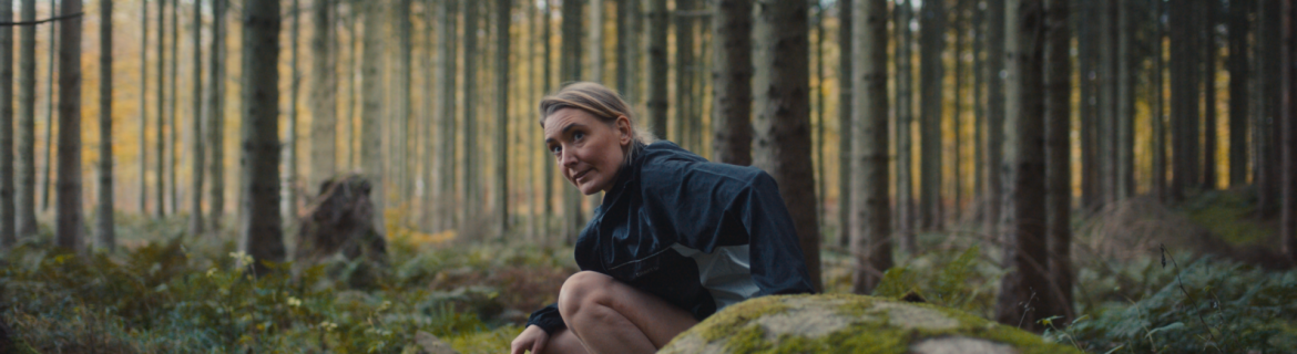 Kvinna som sitter bakom en sten i skogen Kvinna som sitter bakom en sten i skogen